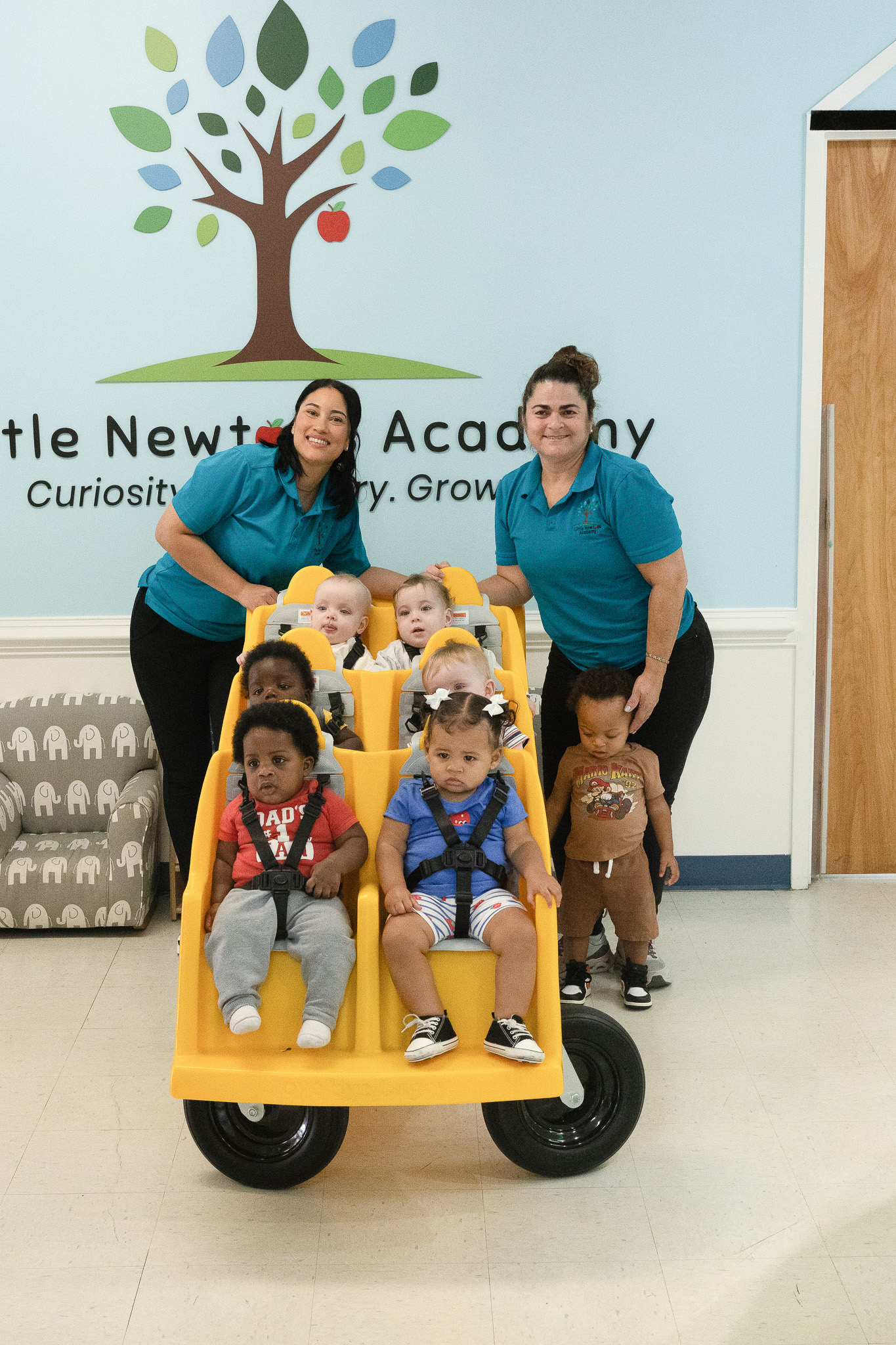 Infants in our buggy in front of the Little Newtons Academy logo wall