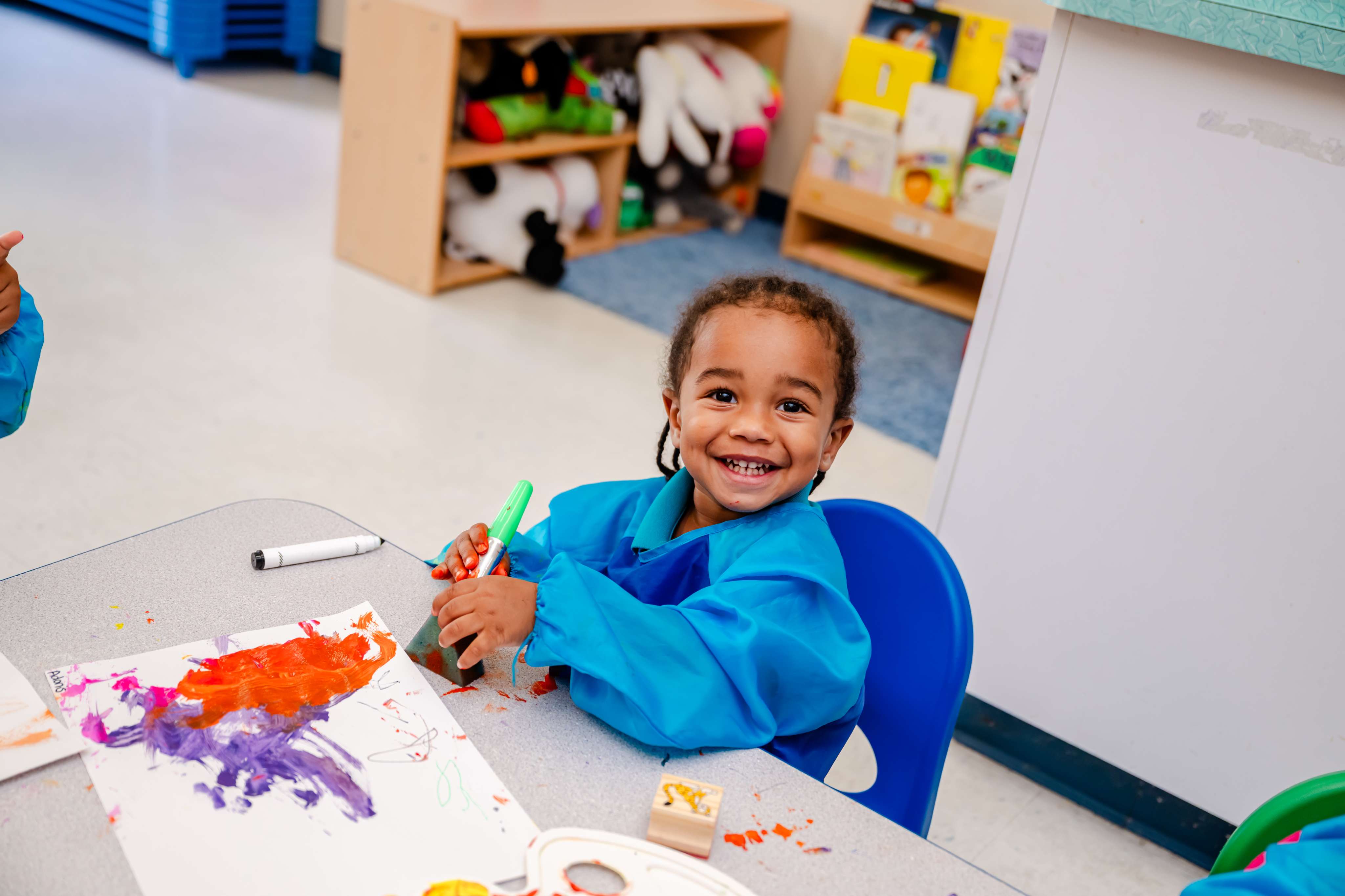 A smiling child painting during an art activity at Little Newtons Academy