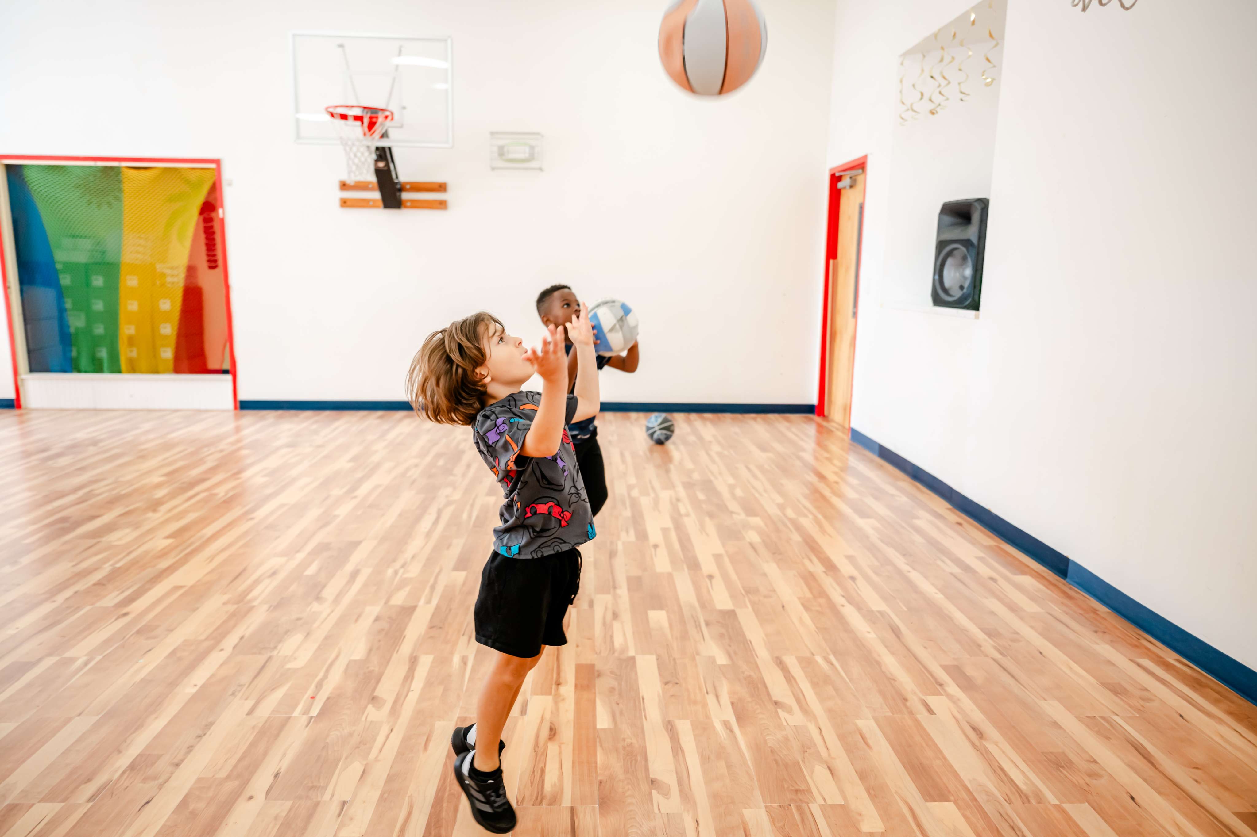 Two children shooting hoops in the indoor gymnasium at Little Newtons Academy Heathrow