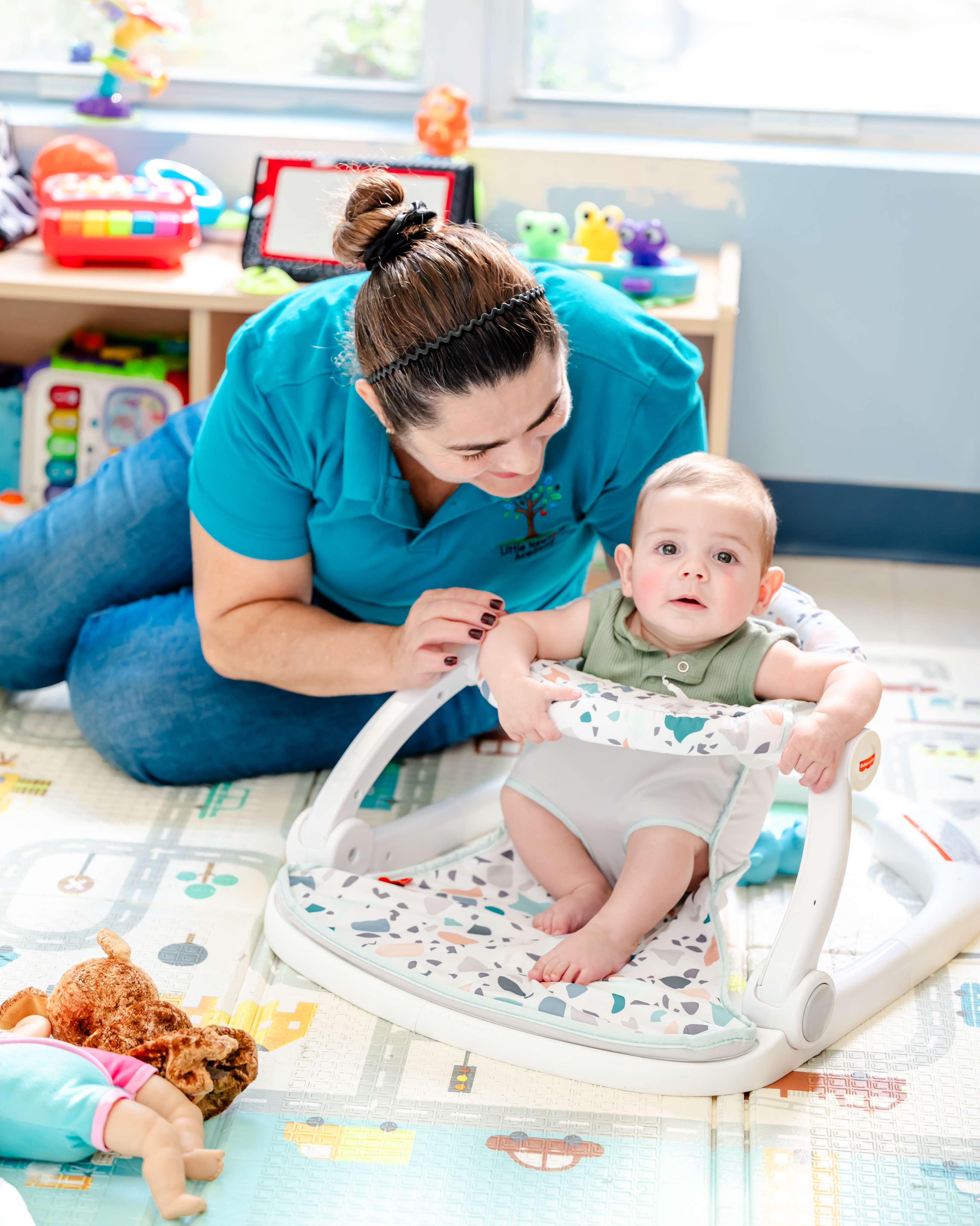 A teacher caring for an infant in a floor seat on a soft play mat at Little Newtons Academy Heathrow